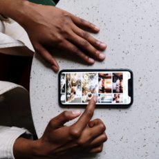 Black woman's hands beside her smartphone scrolling through Instagram images