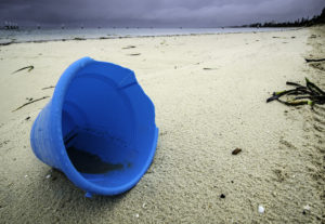 Blue plastic bucket, with bits missing from the top, on deserted beach 