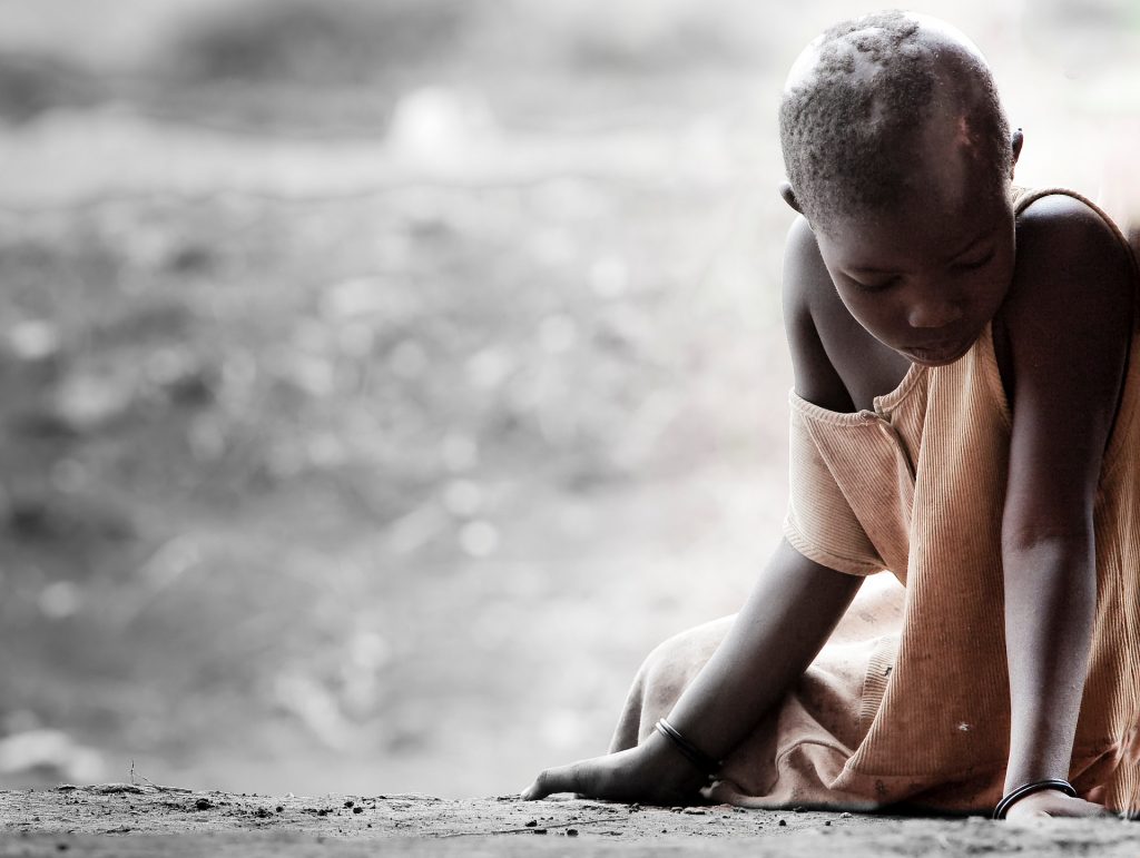 African child in dirty shirt gazing down at the ground. 