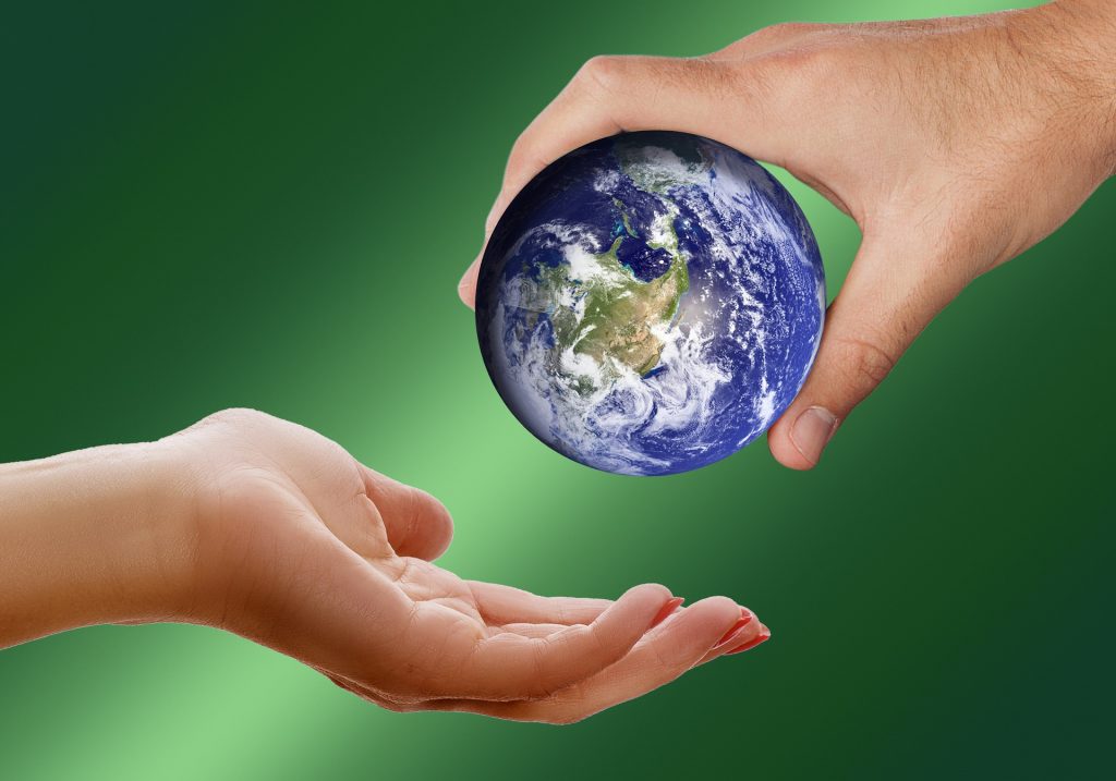 One male hand holding the Earth and placing it in the palm of a female hand with red nail polish. Green background.