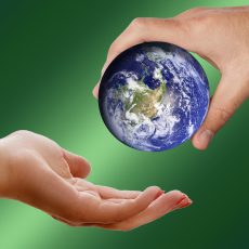 One hand passing a miniature Earth to another hand, green background.