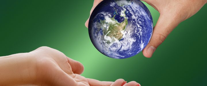 One hand passing a miniature Earth to another hand, green background.