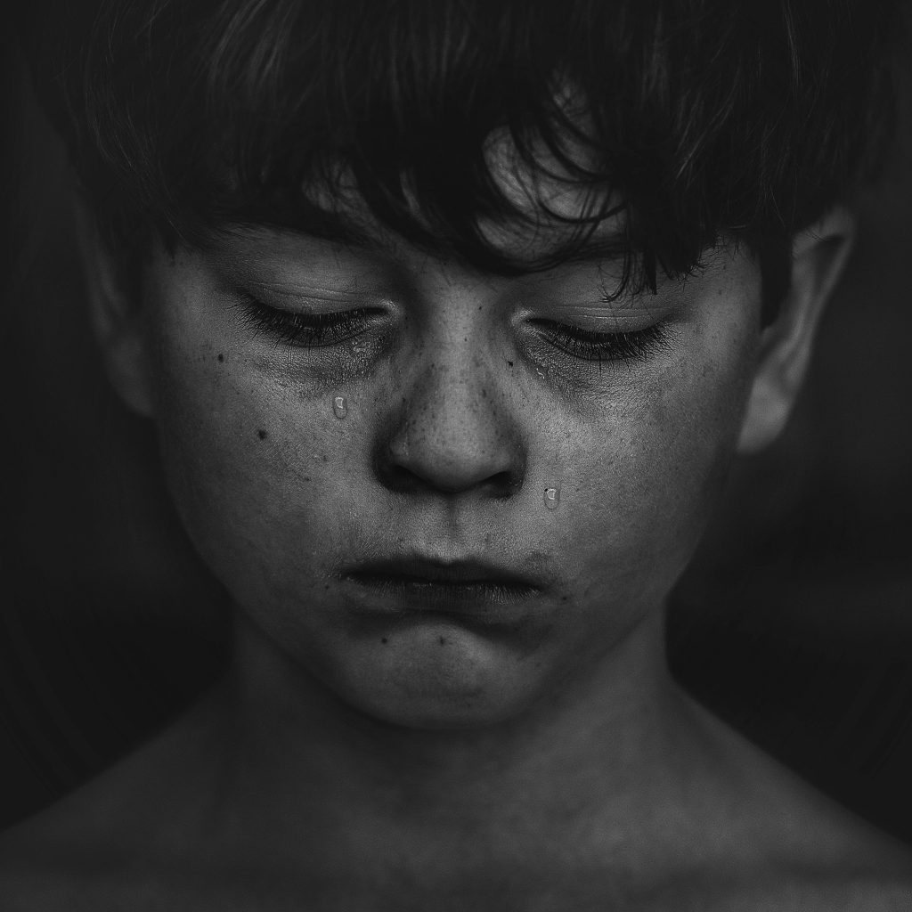 Black and white photo of young boy, downcast, grubby and tears running down his face. 