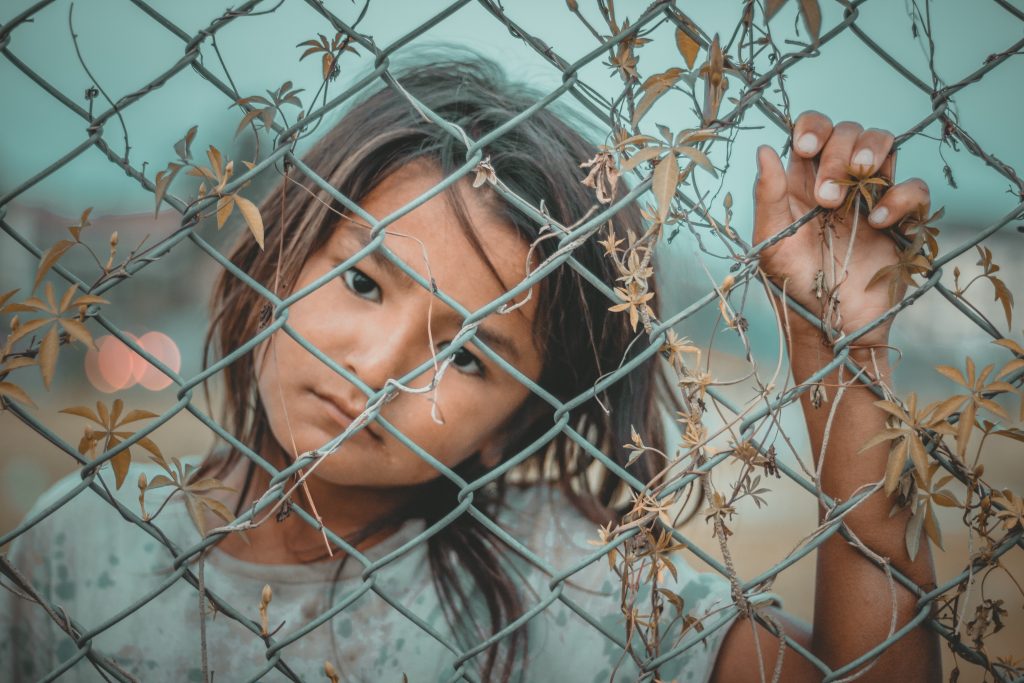 Sad little girl behind chain link fence. 