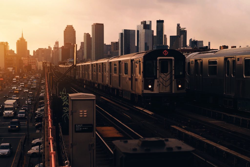 Two New York City #7 trains passing each other as the sun sets over the NYC skyline. 