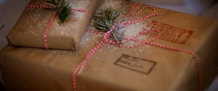 Two packages, one small and one larger, wrapped in simple brown paper and tied with red and white bakery string. Finished with pin sprigs.