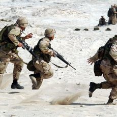 Soldiers running through sand, with weapons