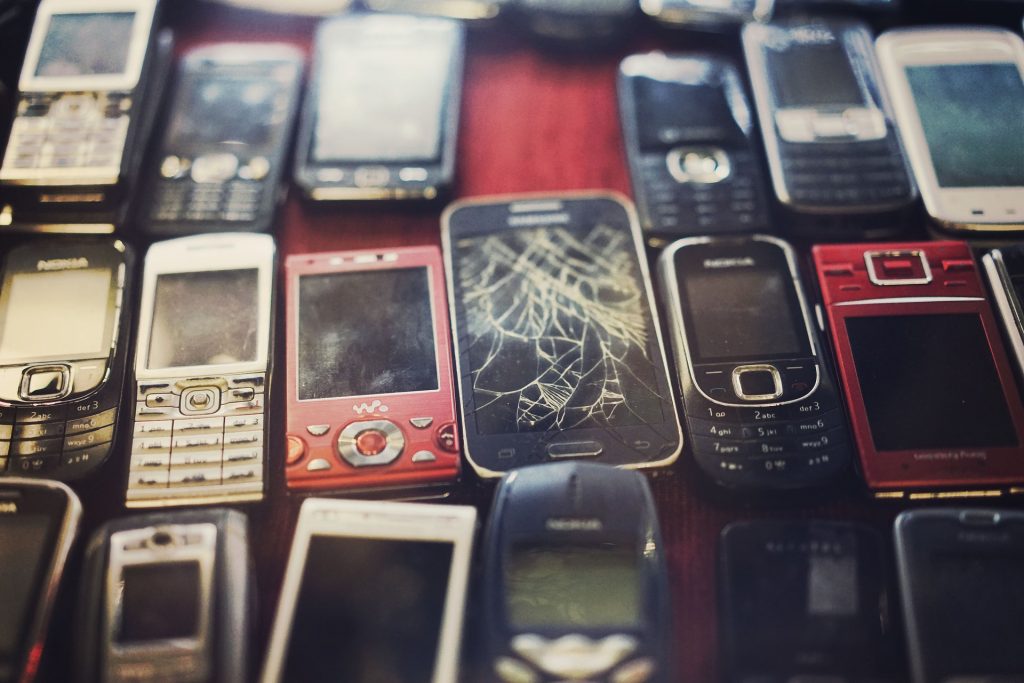 Rows of old cell phones, some with cracked screens. 