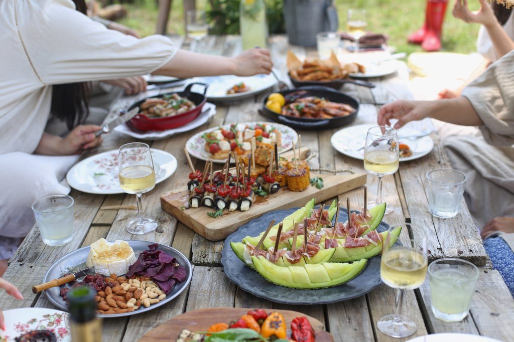 Table setting with food and drinks and people's arms reaching to share it