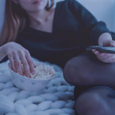 Woman holding a remote control watching tv with a bowl of popcorn