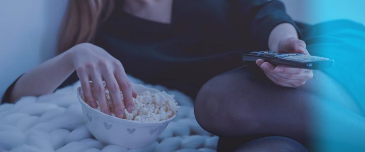 Woman holding a remote control watching tv with a bowl of popcorn
