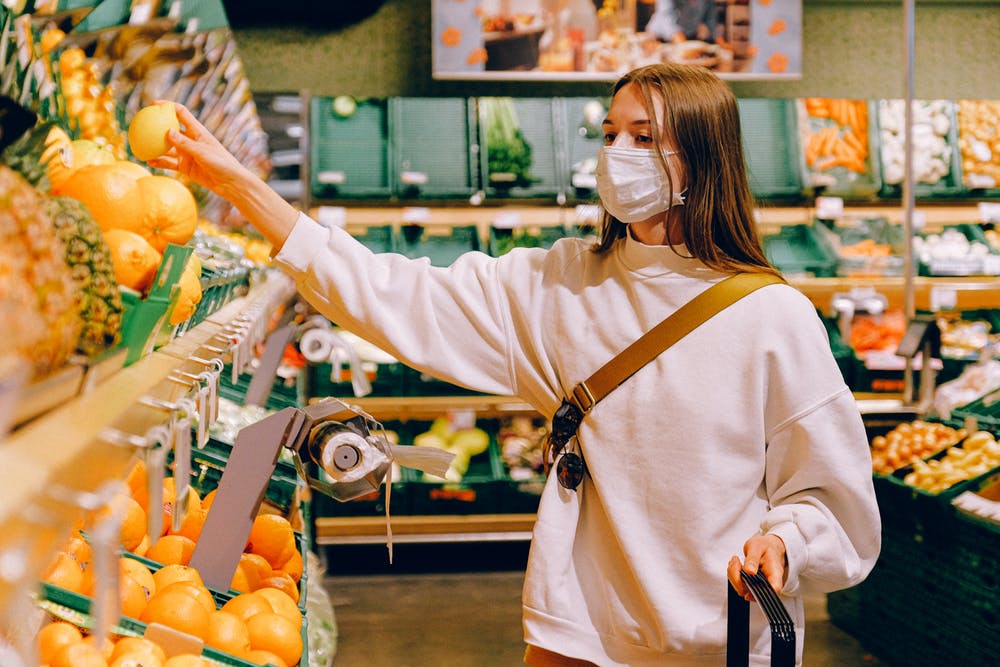 Woman with mask on shopping for fruit. Single use plastic come back for COVID