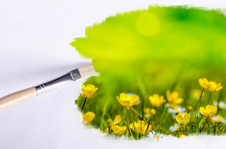 Paintbrush painting a scene of green grass and yellow flowers