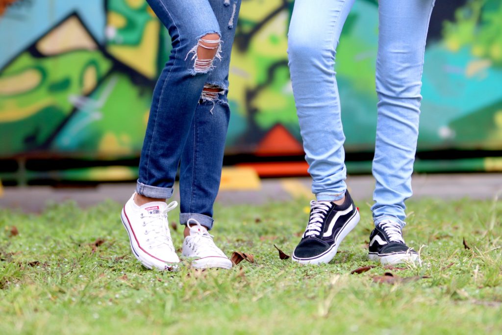 Two people wearing blue denim jeans, showing their legs only, standing in front of graffiti