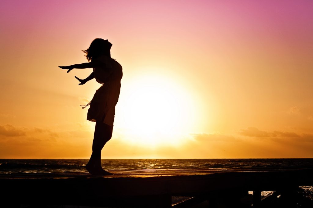 Woman on the beach at sunset throwing her arms open and looking up toward the sky
