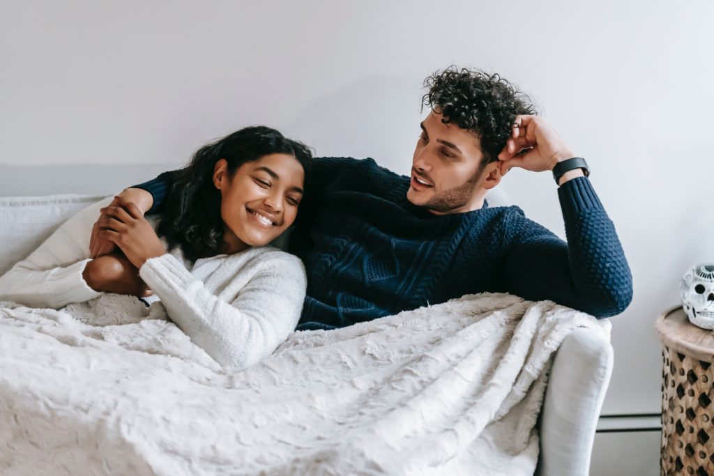 Man and woman cuddling and lounging on a sofa under a blanket to save energy and not use the heating