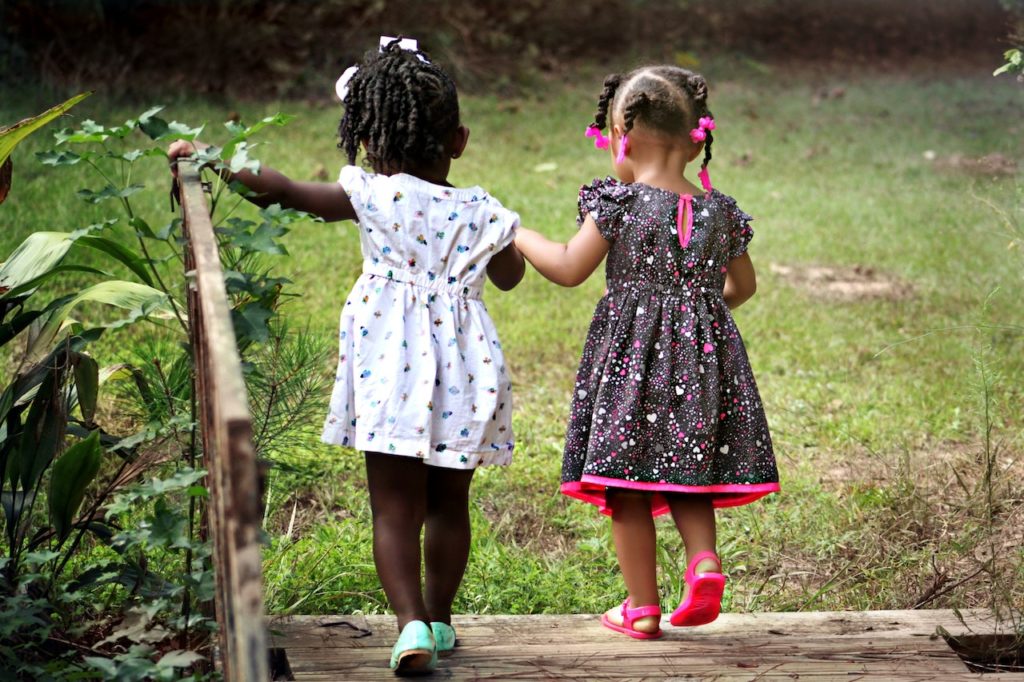 Two little black girls walking over a wooden bridge together holding hands