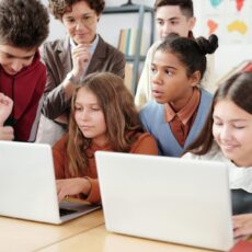 Group of students looking at laptops with teacher in the background