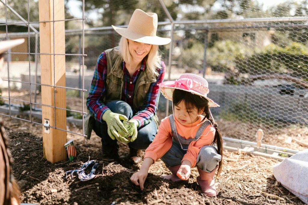 Woman of caucasian background teaching young female child of Asian background to plant seeds in the garden.